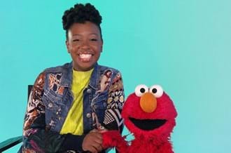 Place2Be Ambassador YolanDa Brown sitting with Sesame Street's Elmo, both smiling at the camera