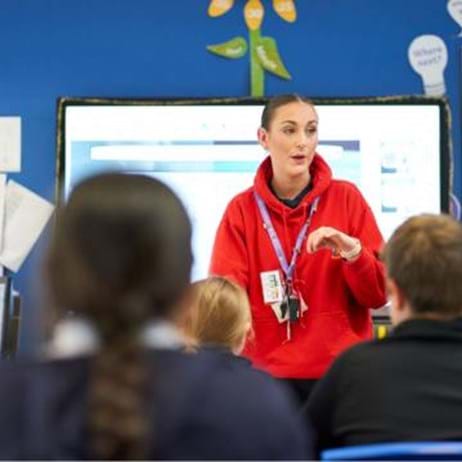 teacher in red hoodie talking to classroom of primary school pupils