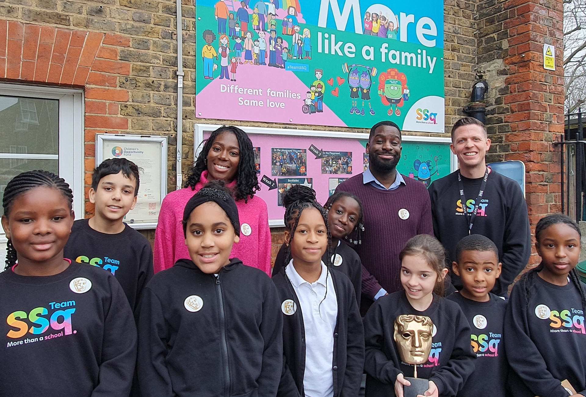 Presenters Shanequa Paris and Inel Tomlinson photographed smiling outdoors with Surrey Square Primary students and Head Teacher Matt Morden.