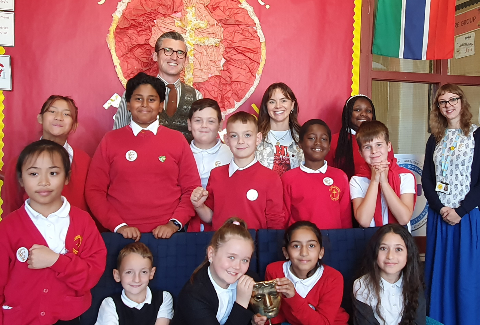 Students from St John Vianney RC Primary standing on school grounds with presenters Ben Shires and Robyn Richford (centre), alongside Place2Be School Project Manager Veronika Medne.