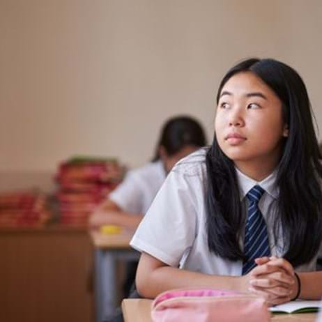 child sat at desk looking out classroom window