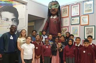 A group St Mary’s CofE Junior and Infant School students smiling, standing alongside BAFTA Roadshow presenters De-Graft Mensah (left) and Kia Pegg (right). 