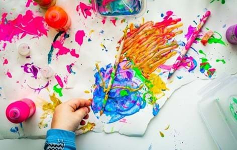 child's hand playing with brightly coloured paint