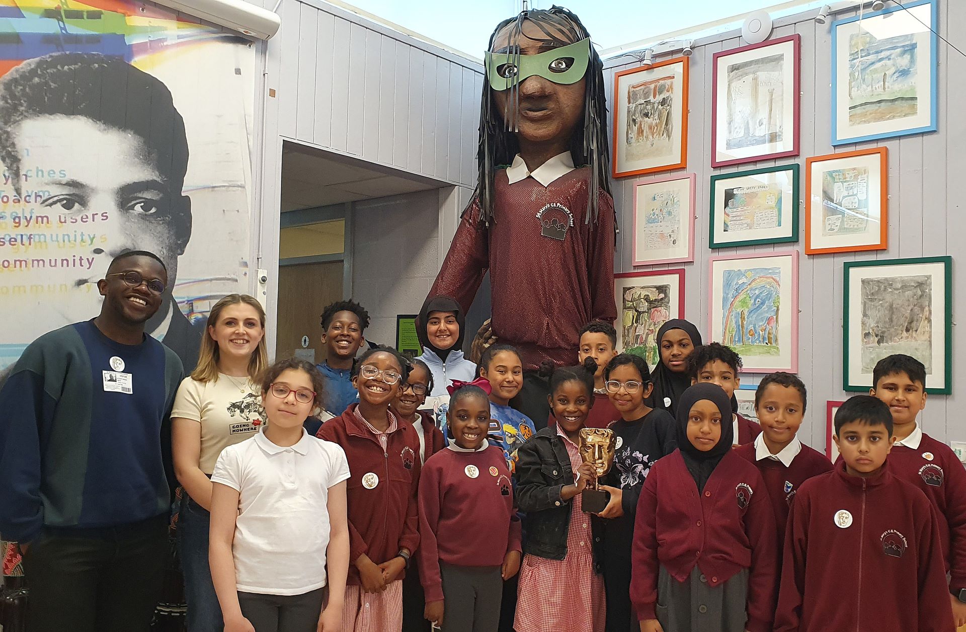 A group St Mary’s CofE Junior and Infant School smiling, standing alongside BAFTA Roadshow presenters De-Graft Mensah (left) and Kia Pegg (right).