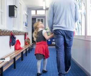 child in school uniform walking down school hallway holding hands of parent