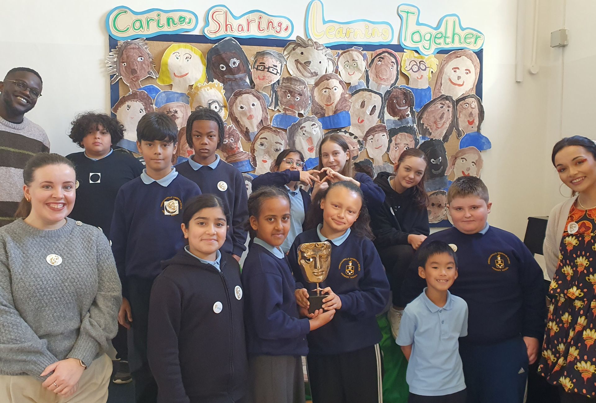 De-Graft Mensah and Mirain Iwerydd standing in a classroom with smiling Tredegarville C.I.W. Primary School students.